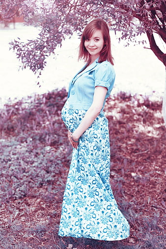 Pregnant woman in blue floral dress standing outdoors