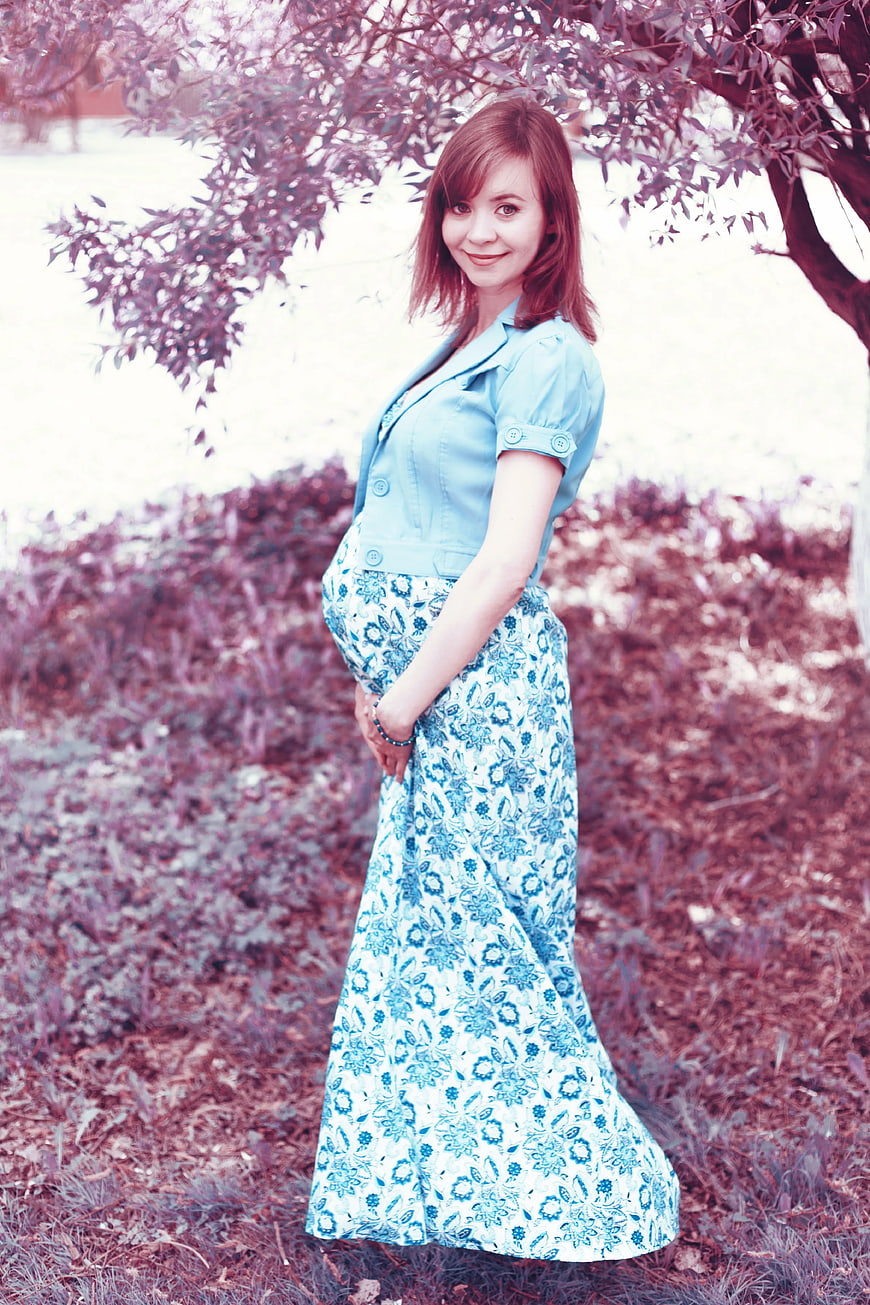 Pregnant woman in blue floral dress standing outdoors