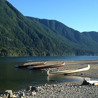 Traditional Canoes on Rocky Shore with Mountain Lake Background