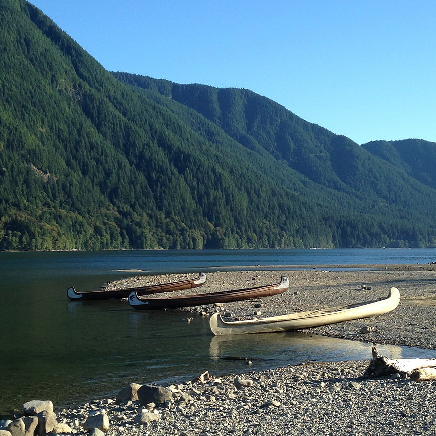 Traditional Canoes on Rocky Shore with Mountain Lake Background