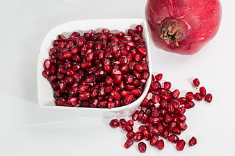 Fresh Pomegranate Seeds in White Bowl with Whole Fruit