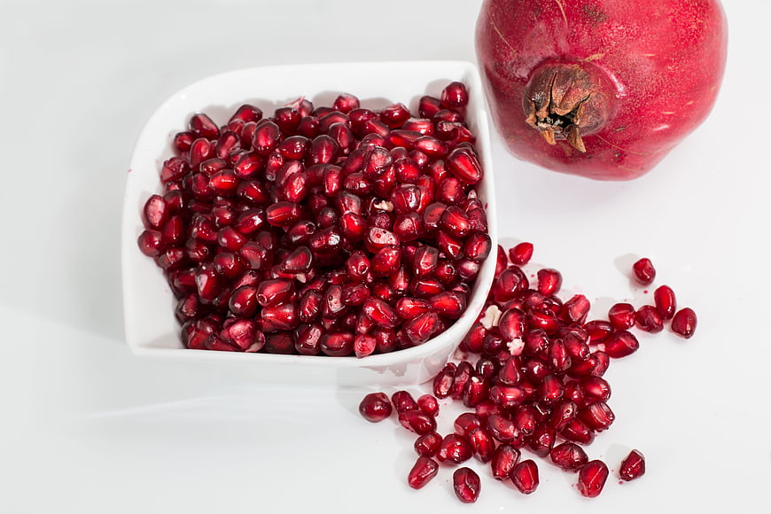 Fresh Pomegranate Seeds in White Bowl with Whole Fruit