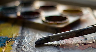 Close-up of paintbrush on textured canvas with blurred palette