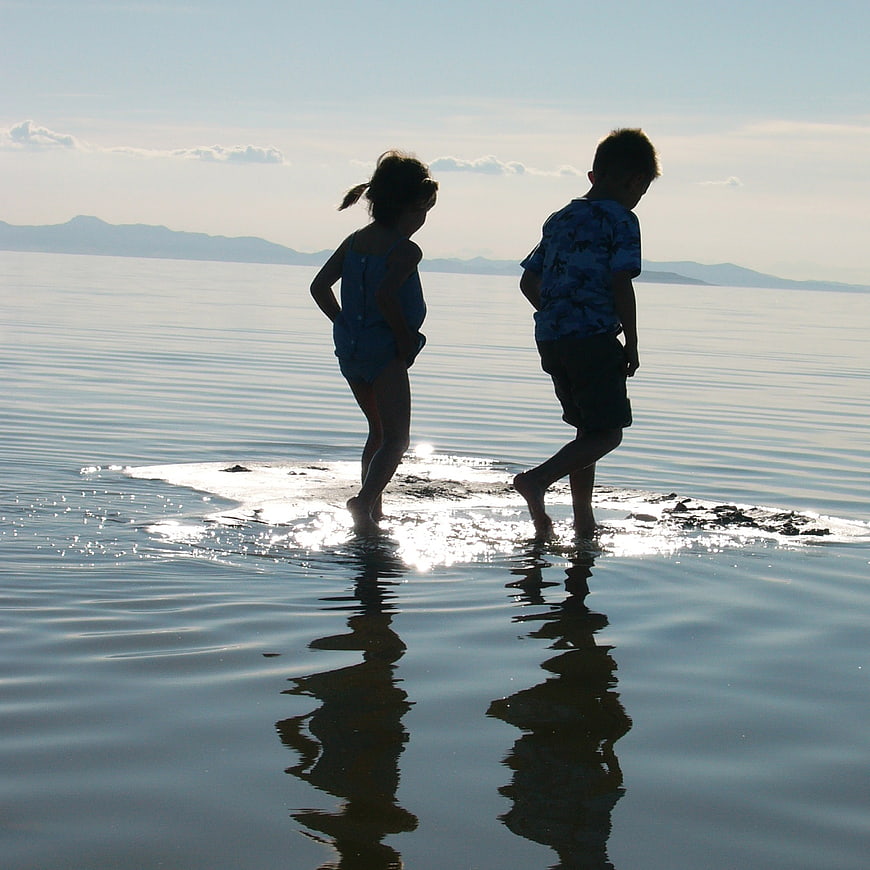 Two children walking in shallow water with reflections