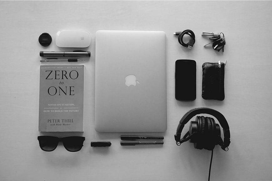 Black and white flat lay of MacBook and startup essentials