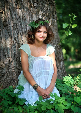 Woman in White Dress with Leaf Crown Sitting by Tree