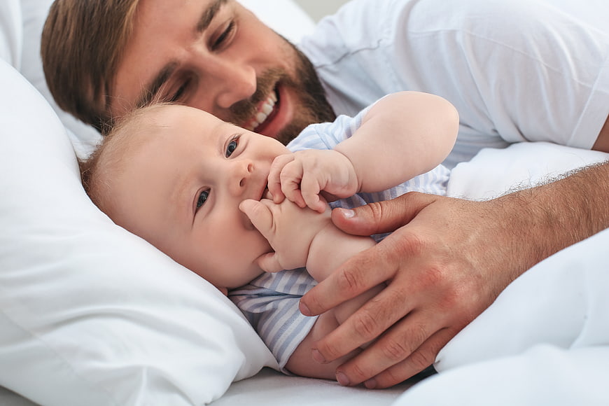 Happy Father Holding Smiling Newborn Baby in Bed