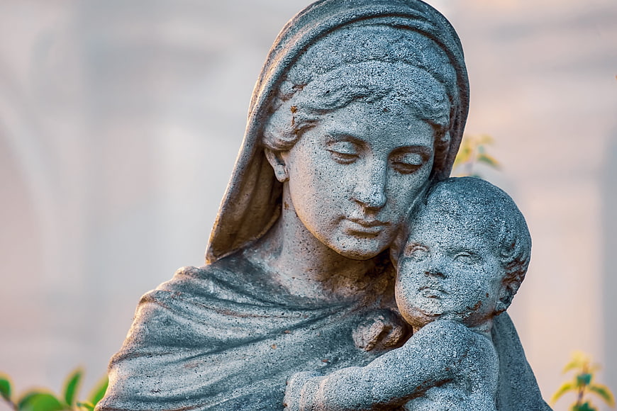 Close-up of weathered stone statue of Mary and child in soft light