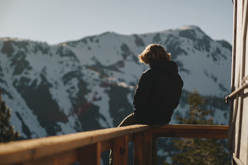 Person sitting on wooden balcony overlooking snowy mountains