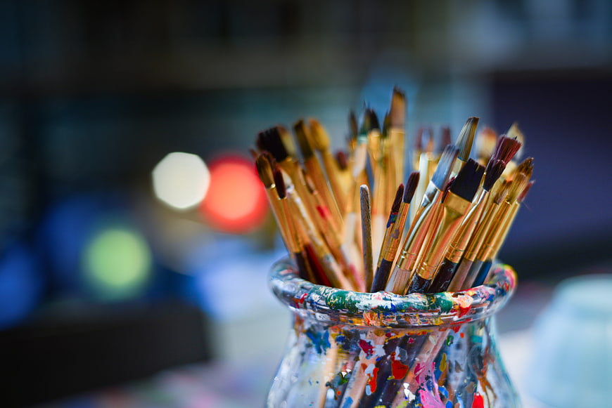 Paintbrushes in a colorful glass jar with blurred studio background