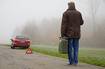 Man carrying fuel canister to broken down car in fog