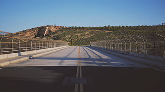 Empty concrete bridge road with chain-link fence and hills
