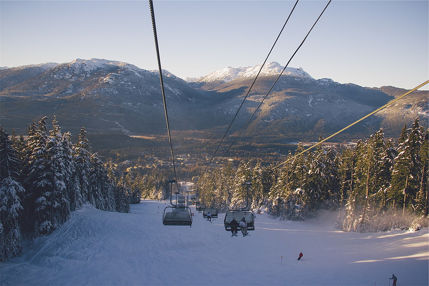 Ski resort chairlift view with snowy mountains and pine trees