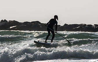 Woman Paddleboarding on Ocean Waves Near Rocky Shoreline