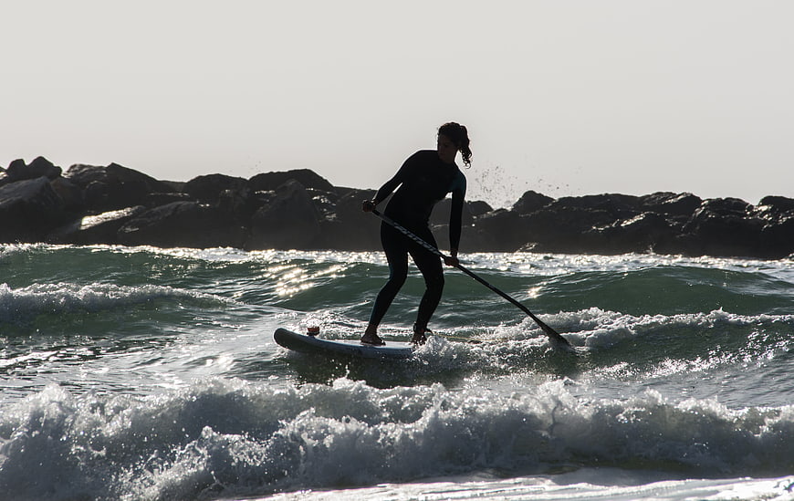 Woman Paddleboarding on Ocean Waves Near Rocky Shoreline
