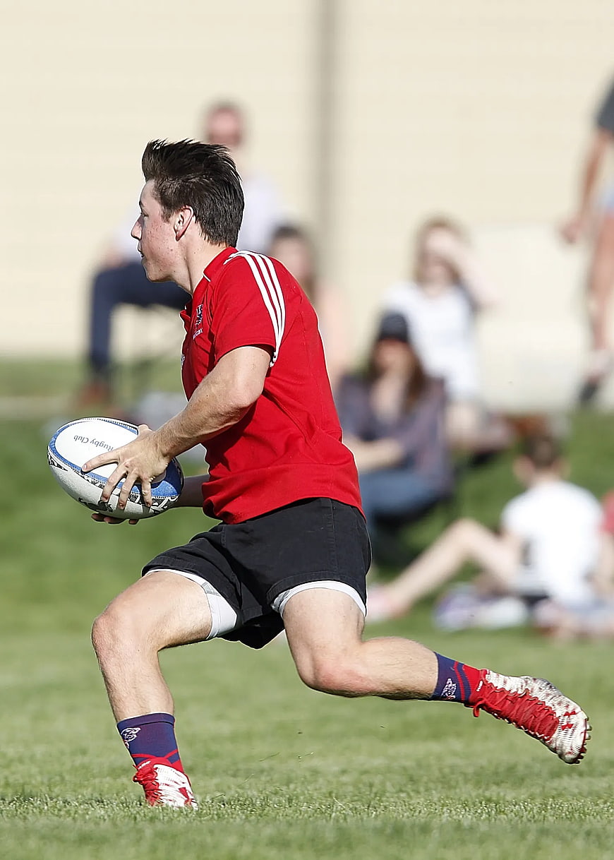 Male Rugby Player Running with Ball on Grass Field