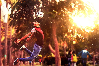 Boy Jumping to Head Soccer Ball in Park at Sunset