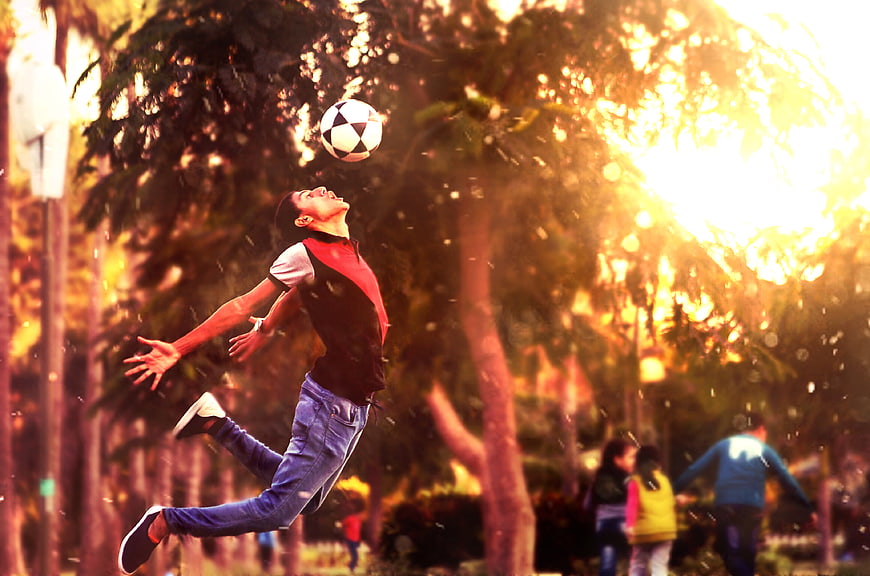 Boy Jumping to Head Soccer Ball in Park at Sunset