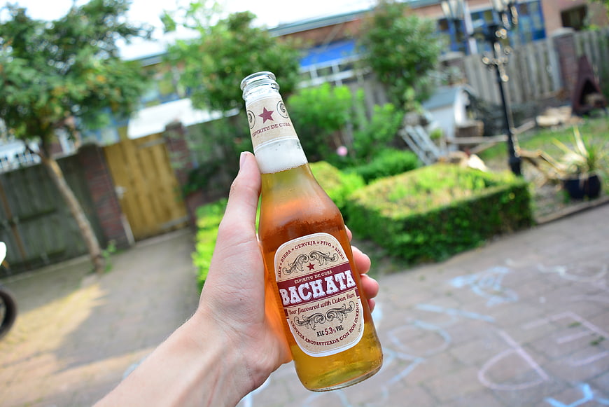 Hand holding Bachata beer bottle in garden