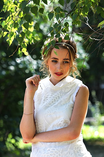Young woman in white lace dress under green leaves