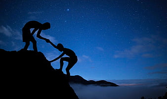 Silhouette of two men helping each other climb a mountain under a starry night sky