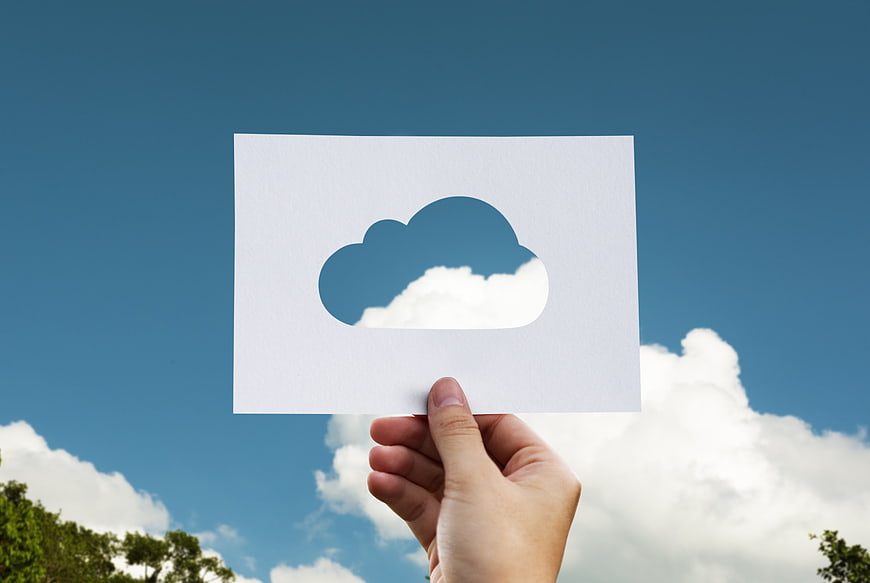 Hand holding paper with cloud cutout against blue sky