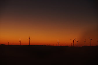 Silhouette of wind turbines against orange sunset sky