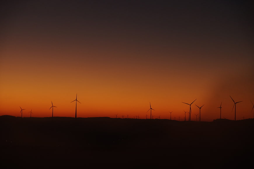 Silhouette of wind turbines against orange sunset sky