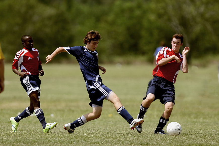 Three Men Playing Soccer on a Grass Field