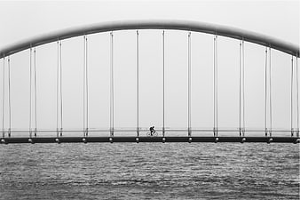Cyclist on modern arched bridge over water in black and white