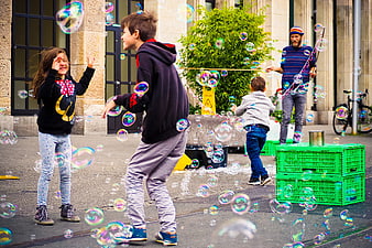 Children playing with giant soap bubbles on city street