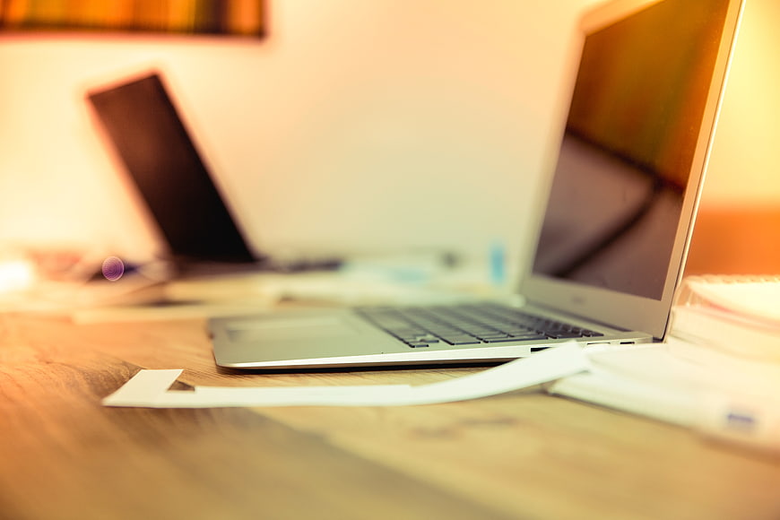 Silver laptop on wooden desk with blurred office background