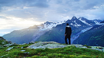 Hiker Standing on Rocky Mountain Summit Overlooking Snowy Peaks