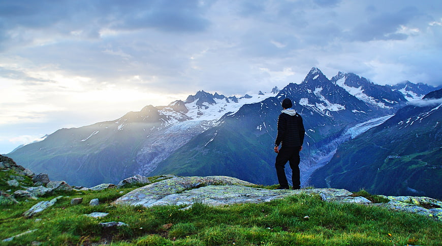 Hiker Standing on Rocky Mountain Summit Overlooking Snowy Peaks