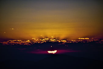 Dramatic Sunrise Over Silhouetted Mountains with Golden Clouds
