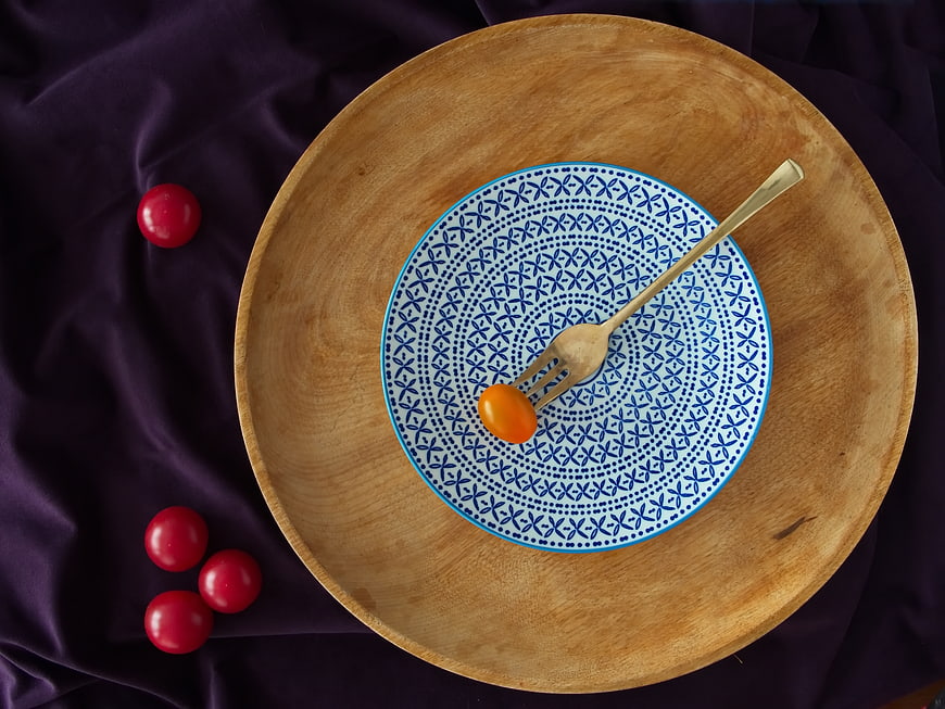 Flat lay of wooden bowl with blue patterned plate and cherry tomatoes
