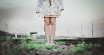 Woman standing barefoot on overgrown railway tracks
