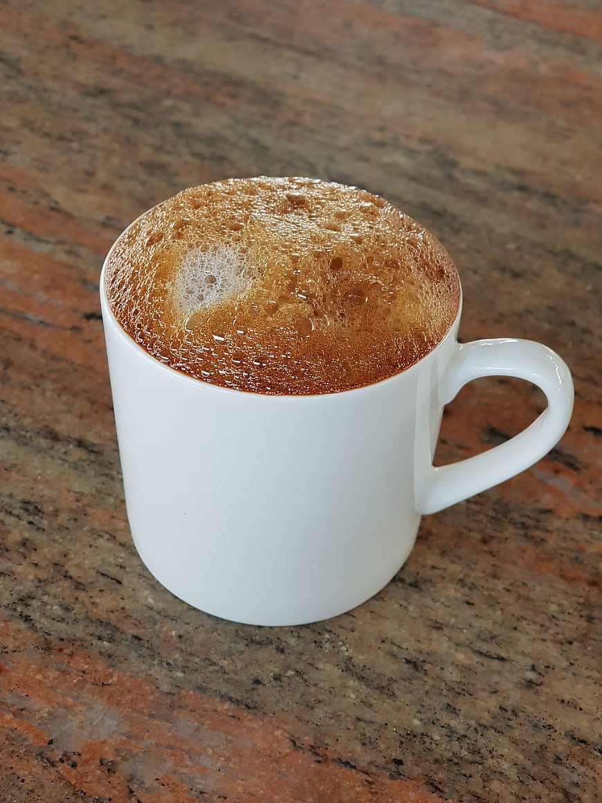 Close-up of frothy coffee in a white ceramic mug on granite