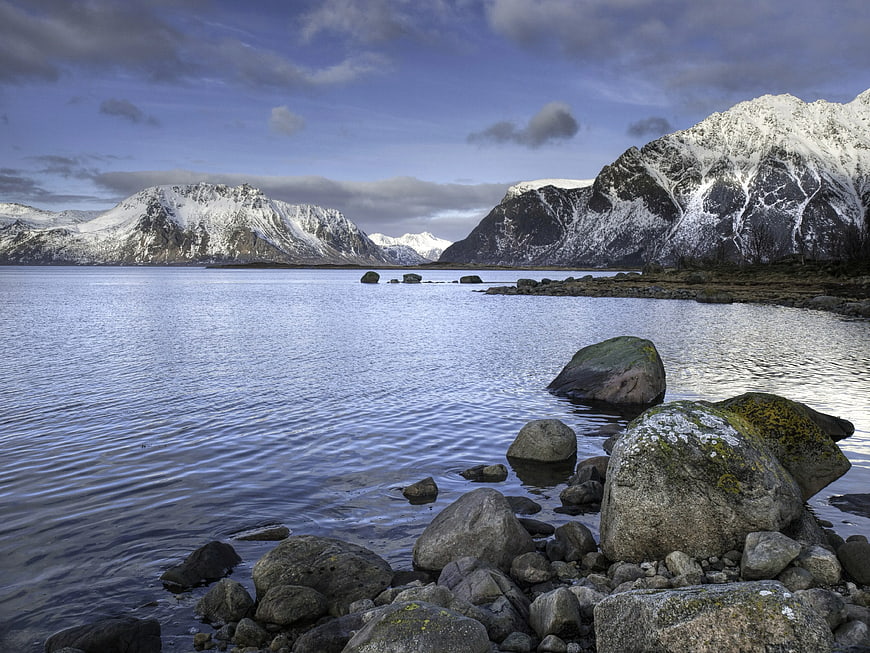 Snow-Capped Mountains and Rocky Shoreline by Blue Water