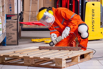 Warehouse worker grinding wood pallet with angle grinder
