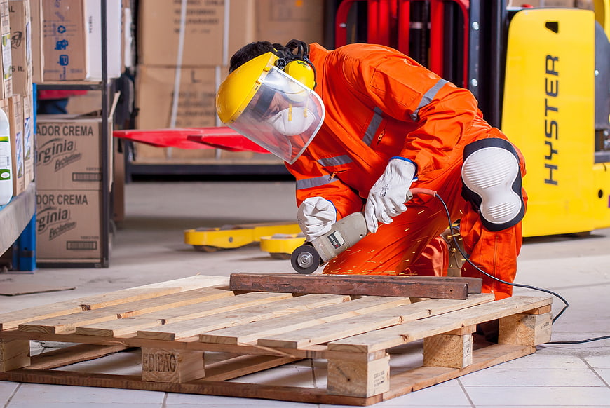 Warehouse worker grinding wood pallet with angle grinder