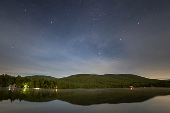 Starry Night Sky Over Lake and Forested Mountains