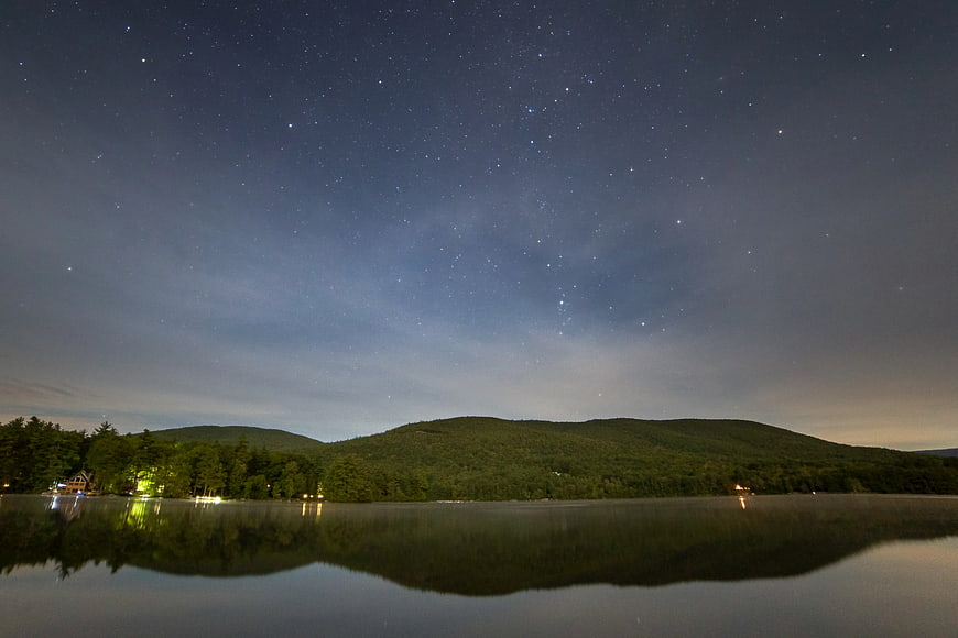 Starry Night Sky Over Lake and Forested Mountains