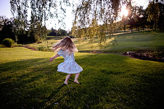 Little girl running barefoot in grassy park at sunset