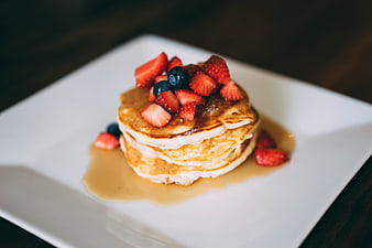 Stack of pancakes with strawberries and blueberries on white plate