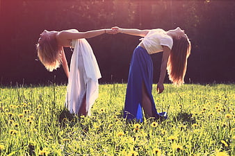 Two women holding hands in a sunny meadow with dandelions