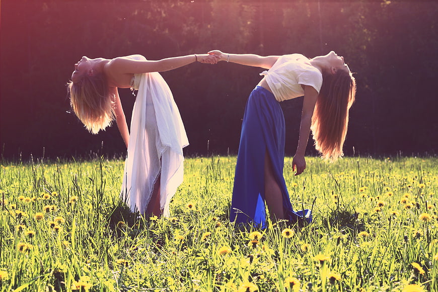 Two women holding hands in a sunny meadow with dandelions