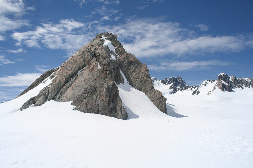 Snowy mountain peak with rocky outcrop under blue sky