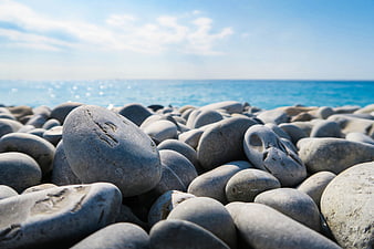 Close-up of smooth gray pebbles on a sunny beach with blue ocean background