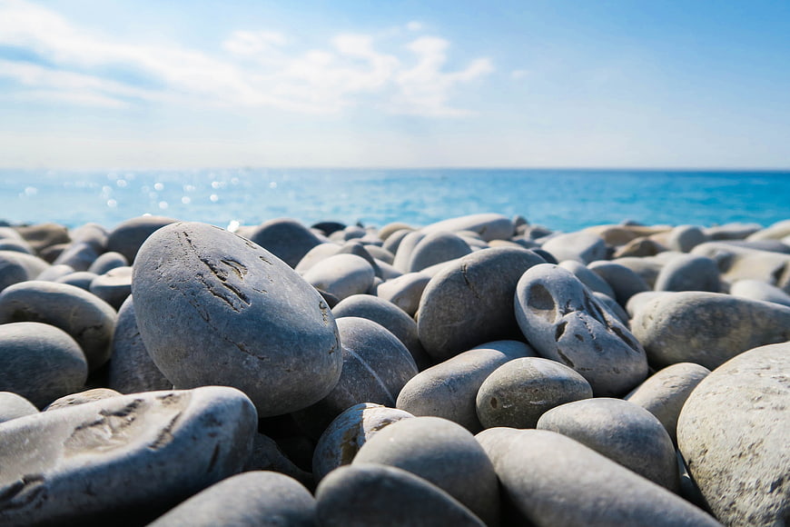 Close-up of smooth gray pebbles on a sunny beach with blue ocean background